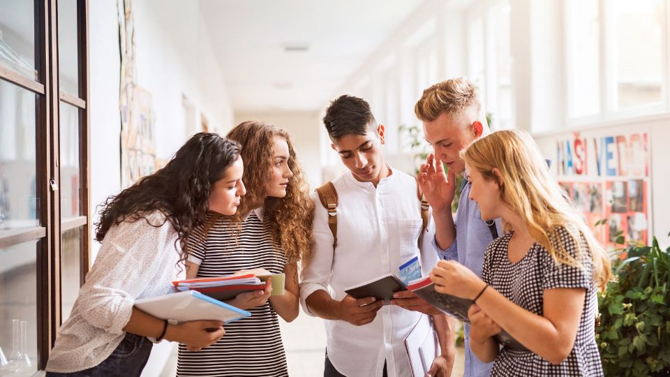 Groupe d'étudiants discutant de logements ensemble dans un couloir lumineux.