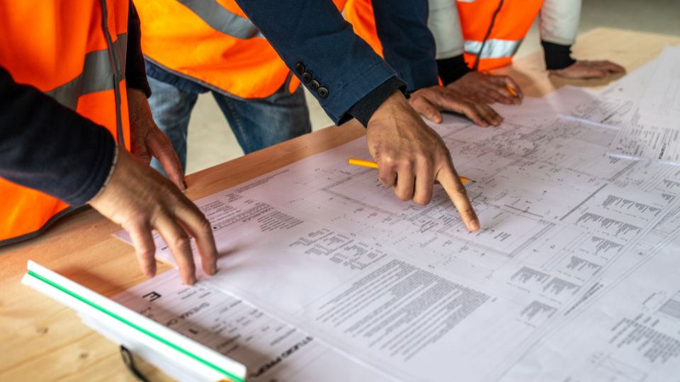 Des personnes en gilets de sécurité orange examinant des plans de construction sur une table.