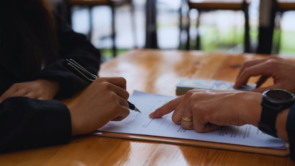 Un conseiller financier aide un client à signer un contrat de prêt sur une table en bois.